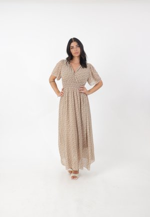 Robe maxi en beige clair avec un motif floral, manches courtes bouffantes, décolleté en V et taille élastique. Portée avec des sandales à talons carrés blanc cassé.