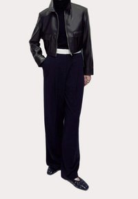 Veste courte en cuir noir, ceinture blanche, pantalon large marine, et chaussures slip-on noires à clous blancs. Texture lisse partout.
