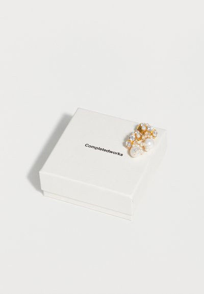 Σκουλαρίκια σε χρυσό χρώμα με μαργαριτάρια και κρυστάλλους, τοποθετημένα πάνω σε λευκό κουτί κοσμημάτων Completedworks πάνω σε λευκό φόντο.