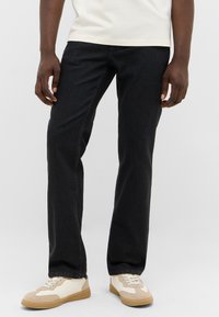 Black denim jeans with a straight-leg fit, cotton material, subtle texture, and stitched seams, paired with cream and beige sneakers.