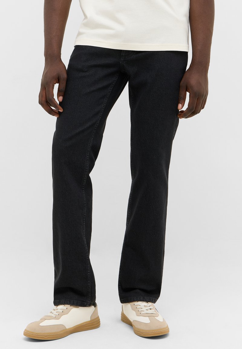 Black denim jeans with a straight-leg fit, cotton material, subtle texture, and stitched seams, paired with cream and beige sneakers.