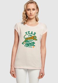 Lichtroze T-shirt met opgerolde mouwen, voorzien van een tijgerafbeelding en tekst "JAAR van de Tijger" in groen en oranje. Katoenen materiaal.