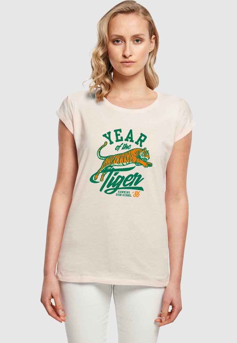 Lichtroze T-shirt met opgerolde mouwen, voorzien van een tijgerafbeelding en tekst "JAAR van de Tijger" in groen en oranje. Katoenen materiaal.