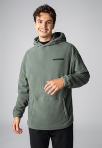 Fleece-Kapuze in Olivgrün mit Fronttasche, verstellbarer Kordelzugkapuze und schwarzem "WORLDWIDE"-Aufdruck auf der Brust.