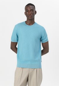 Svetlo modra kratka pletena majica s kratkimi rokavi, okrogel izrez, rebrasti manšeti in rob, značilna po teksturirani vzorčni površini.