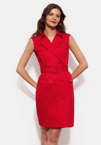 Czerwona sukienka bez rękawów z paskiem w talii, podwójnym zapięciem z przodu i dwiema kieszeniami z przodu. Wykonana z gładkiego materiału o dopasowanym kroju.