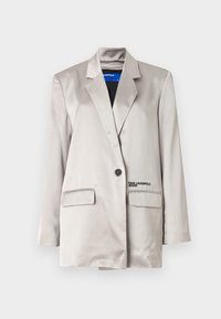 Lys beige blazer i satengfabric, med en enkelt knappelukking, to lommer og subtil merking på venstre lomme.