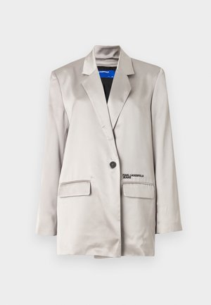 Lys beige blazer i satengfabric, med en enkelt knappelukking, to lommer og subtil merking på venstre lomme.