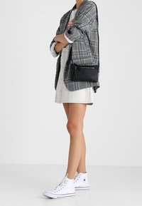 Harmaa ruudullinen bleiseri valkoisen t-paidan päällä, yhdistetty farkkuhameeseen ja valkoisiin korkeavartisiin tennareihin. Musta olkalaukku, jossa vetoketjusomiste.