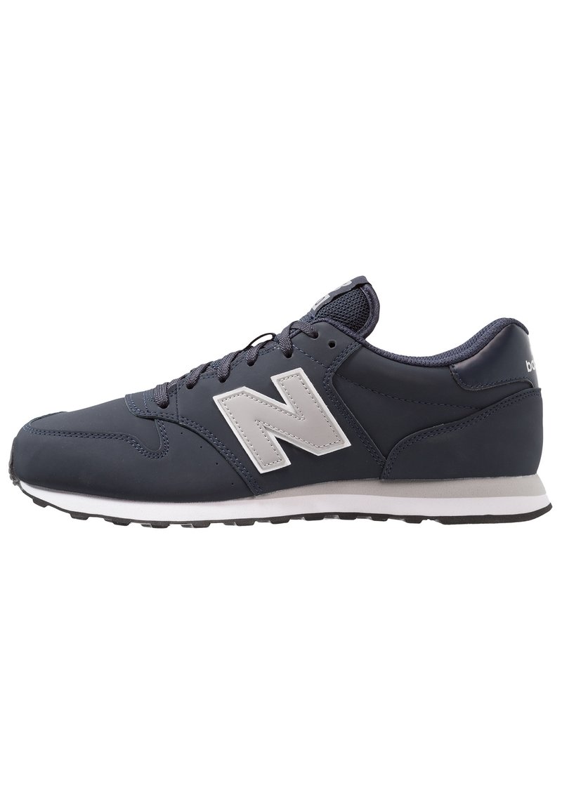 Zapatilla deportiva de color azul marino con parte superior de malla y sintético, logo blanco, cierre con cordones y suela de goma negra. Presenta una puntera redondeada y un cuello acolchado.
