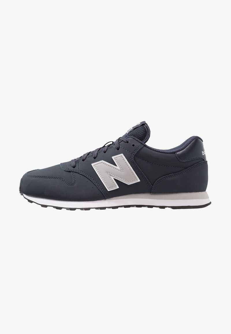 Zapatilla deportiva de color azul marino con parte superior de malla y sintético, logo blanco, cierre con cordones y suela de goma negra. Presenta una puntera redondeada y un cuello acolchado.
