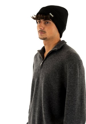 Berretto in maglia nera e pullover in pile grigio antracite con collo con zip. Il tessuto è morbido, con accenti a coste sul colletto del maglione.