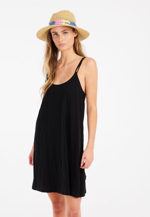 Schwarzes ärmelloses Kleid mit dünnen Trägern, aus leichtem Stoff gefertigt. Kombiniert mit einem Strohhut, der ein mehrfarbiges gewobenes Band hat.