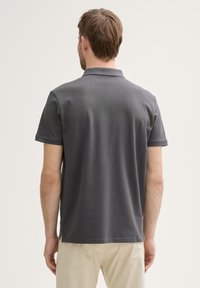 Mørkegrå polo t-shirt med korte ærmer, flad krave og slidser i siderne ved kanten. Glat stoftekstur med en let glans.