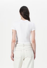 Hvit kortermet croppet t-skjorte laget av myk stoff, kombinert med lyse denimhøytalede bukser. Enkel design, ingen mønstre.
