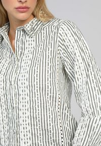 Chemise à rayures blanche et verte, dotée d'un tissu texturé, de coutures décoratives et d'un col orné.