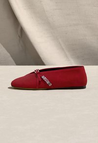 Chaussure plate rouge à bout pointu, bride latérale avec deux boucles argentées et lettrage métallique de la marque MOSCHINO.