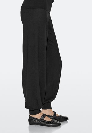 Pantaloni jogger neri, larghi, con polsini elastici, abbinati a ballerine nere con texture arricciata e dettaglio ritagliato.