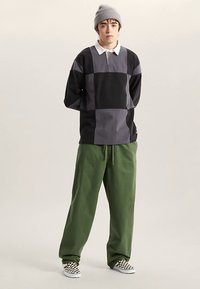 Langærmet, sort og gråt farveblokeret top med en hvid krave, kombineret med løse grønne bukser og sko med sort-hvidt ternet mønster.