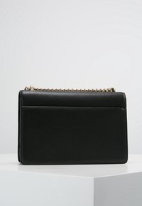 Borsa a mano in pelle nera con una forma rettangolare strutturata, tracolla a catena e una texture liscia. Presenta un logo sottile impresso sul davanti.