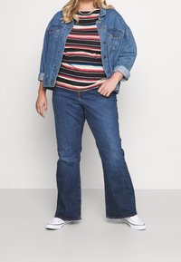 Džínová bunda, pruhované tričko v červené, modré a bílé barvě, rozšířené džínsy a bílé tenisky, s uvolněným střihem a neformálním stylem.