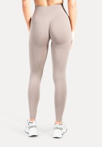 Beige leggings met een hoge taille, een gladde, rekbare textuur en contourvormende pasvorm. Gecombineerd met witte sportschoenen met zwarte accenten.