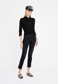 Maglietta nera a maniche lunghe in maglia con dettagli a bottone, abbinata a jeans in denim scuro con orli sfrangiati e ballerine grigie.
