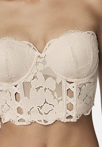 Soutien-gorge sans bretelles en beige clair avec des motifs floraux, soutien-gorge à armatures, et un nœud décoratif au centre, doté d'accents à lacets sur les côtés.