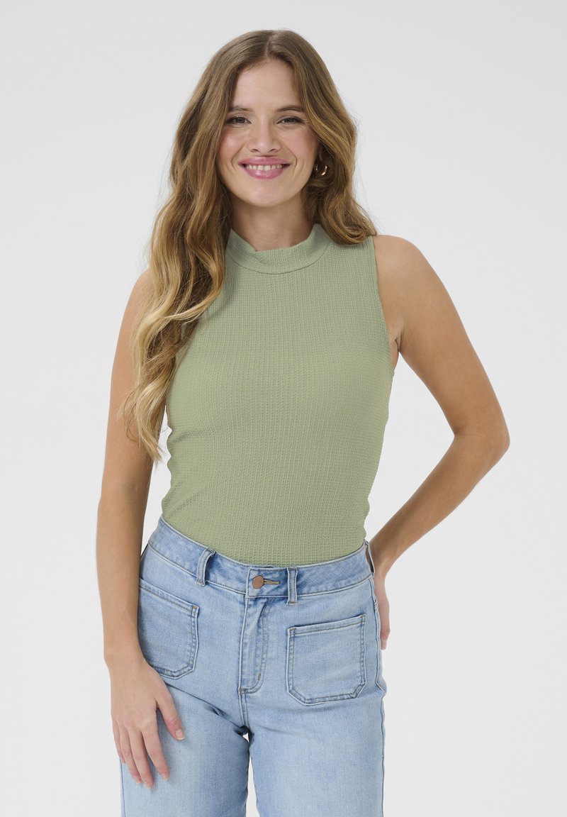 Grön ribbad ärmlös topp med hög hals, i kombination med högmidjade ljusblå denimjeans med bakfickor.