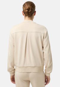 Béžová mikina s pružnými manžetami a lemem, s plisovaným detailem na zádech. Vyrobena z měkké látky, navržena pro pohodlný střih.