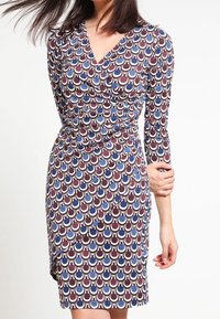 Viktdress i ett geometriskt mönster med vinröda, blå och vita färger. Långa ärmar, V-hals och knälång design. Slät tygtextur.