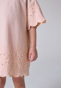 Ružové vyšívané šaty s oblými rukávmi a lemom, s kvetinovými vzormi a výrezmi, jemnou textúrou a voľným strihom.