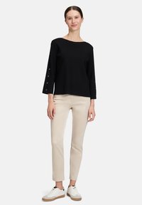 Czarny sweter z rękawami do 3/4 i zapięciami na guziki, w połączeniu z beżowymi spodniami i białymi sneakersami. Prosty, czysty design i swobodny krój.