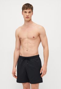 Costume de baie negre, dintr-un material texturat, cu talie elastică și șnur, având o croială lejeră și lungime deasupra genunchiului.