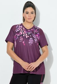 Camiseta de cuello en V morada con un vibrante estampado floral en rosa y blanco, mangas cortas y un corte relajado, combinada con leggings negros.