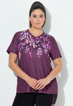 Paarse V-hals T-shirt met een levendige bloemenprint in roze en wit, korte mouwen en een relaxte pasvorm, gecombineerd met zwarte leggings.