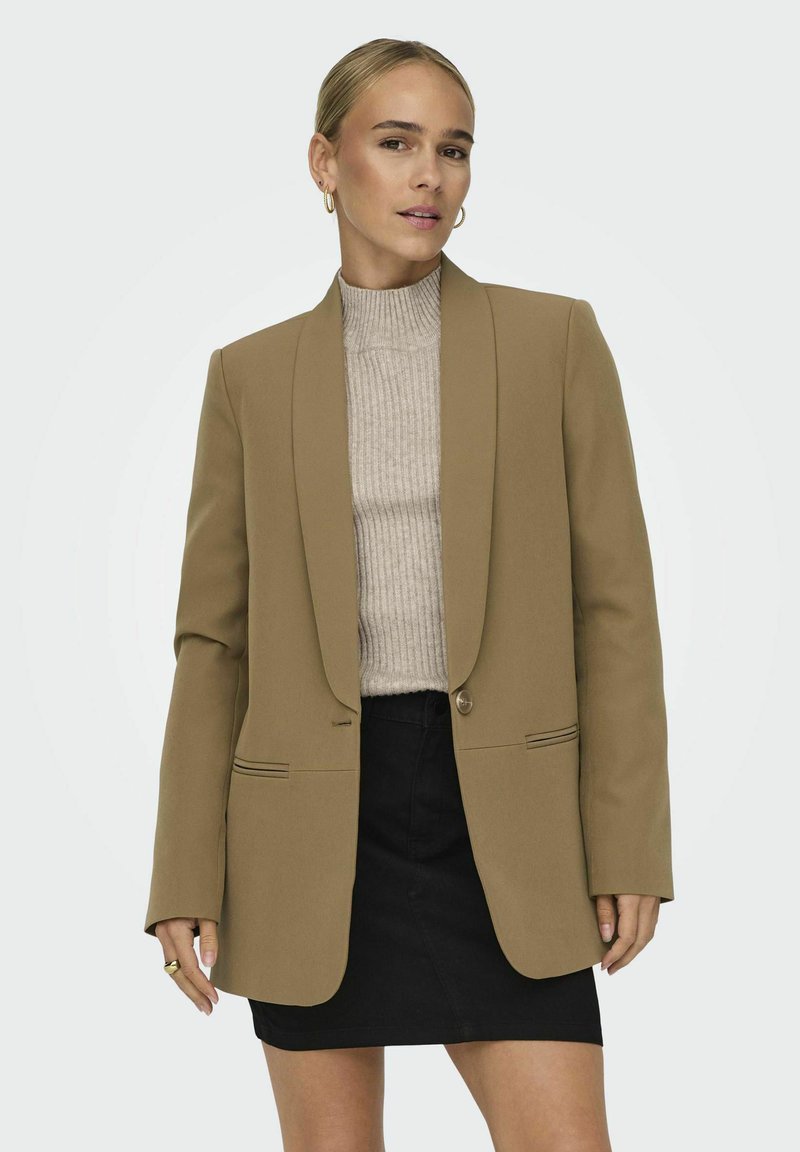 Benvit blazer med spetsiga slag, enfalld knäppning och framfickor, tillsammans med en ribbad beige tröja och svart kjol.