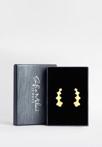 Guldhängande örhängen med en kurvig, länkad design som visas i en svart sammetsklädd låda. Lådan har en strukturerad mörkgrå yta.