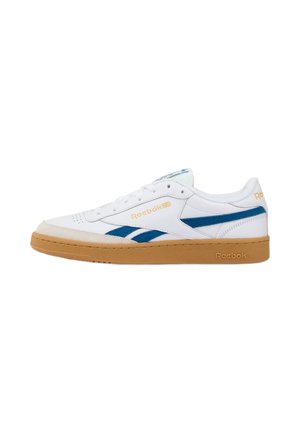 Zapatilla blanca de Reebok con rayas azules, suela de goma marrón claro, diseño con cordones y branding de Reebok en el lateral y en el talón.
