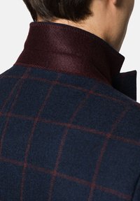 Granatowa kurtka z wełny z domieszką w burgundowym kolorze. Posiada wzór w kratę w kolorach czerwonym i niebieskim, wyróżniając się teksturowanym wykończeniem.