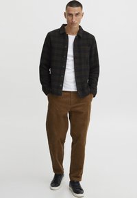 Black and brown plaid flannel shirt with a button-down front and chest pocket, paired with brown corduroy pants and black sneakers.