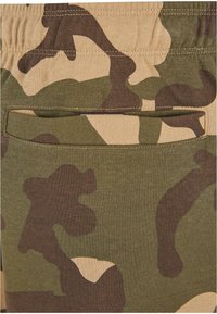 Green and beige camouflage-patterned fabric with a soft texture. Features a back pocket with an open top and stitched edges.