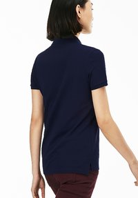 Granatowa koszulka polo o klasycznym designie, z krótkimi rękawami i bocznymi szczelinami. Wykonana z gładkiego materiału bawełnianego, z standardowym kołnierzykiem.