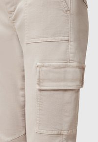 Los pantalones cargo beige presentan una tela texturada, bolsillos laterales y un bolsillo con solapa en el muslo para mayor utilidad.