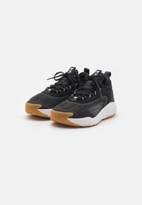 Scarpe sportive nere con tessuto testurizzato, suola in gomma, dettagli arancioni e design con lacci. Presentano il marchio sulla linguetta e sul lato.
