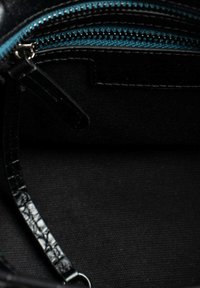 Zwart leren interieur van een tas met een turkwazzipp, een gladde textuur en een klein hengsel. Achtergrond is donker stof zonder patroon.