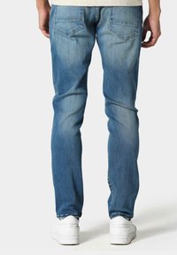 Svetlo modri jeans z ožjim krojem, ki imata dve zadnji žepki in nekoliko zbledel videz. V kombinaciji z belimi supergami.