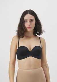 Black strapless bra with a smooth matte finish, molded cups, and adjustable thin straps, paired with a nude high-waisted bottom.