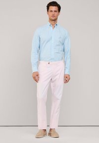 Camisa de botón a rayas azul claro, pantalones rosas, zapatos beiges. La camisa presenta un cuello clásico y un pequeño detalle de logo. Textura suave.