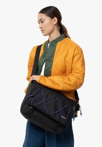 Musta viestilaukku sinisellä koristeropeella, jossa on läppäkiinnitys, säädettävä hihna ja useita osastoja. Valmistettu kestävästä kankaasta.